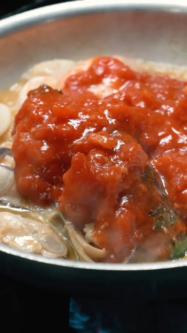 Tomato sauce poured over clams and mussels in the pan