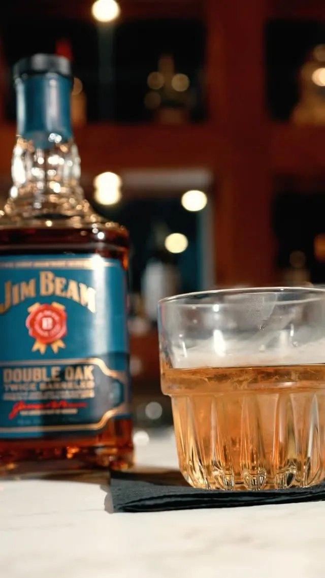 A bourbon on the rocks beside the bottle at the bar