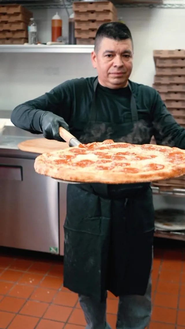 A cook carrying a whole pepperoni pizza out of the Bellini kitchen